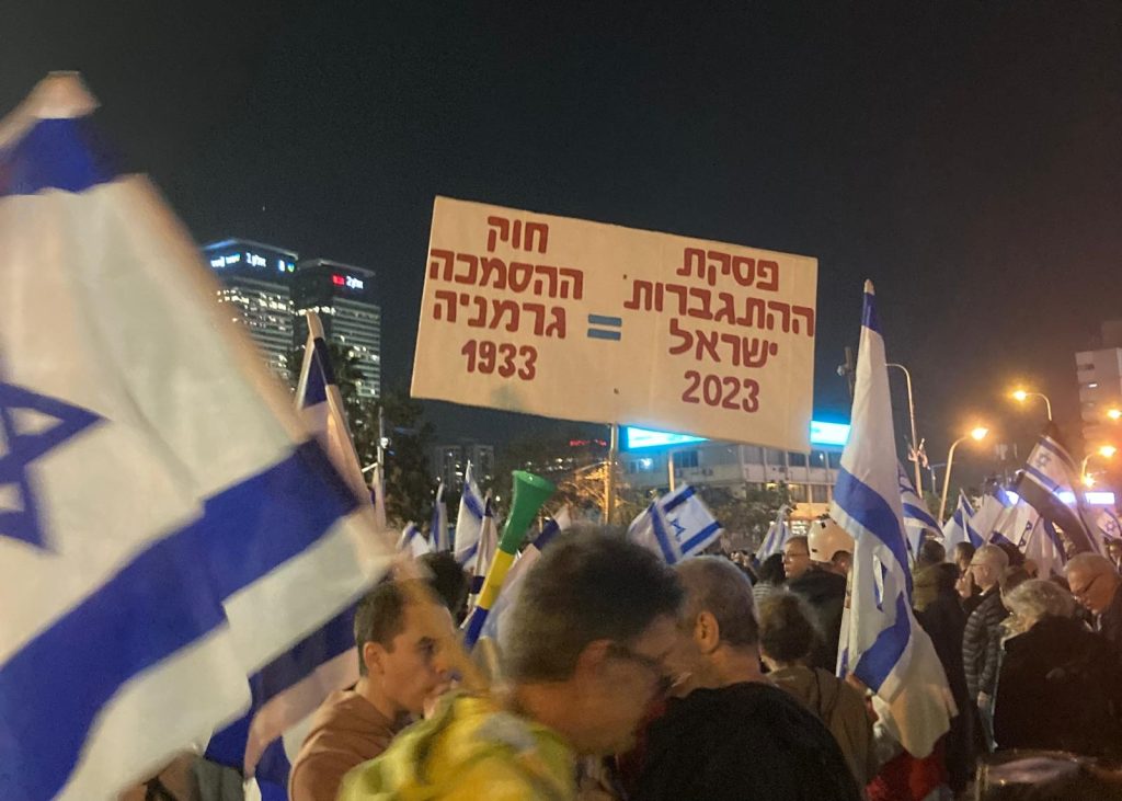 26 Marzo 2023, Tel Aviv. Un manifestante, spaventato dalla crisi costituzionale in Israele, mostra un cartello che equipara il decreto dei pieni poteri promulgato da Hitler nel 1933 al progetto di legge del governo Netanyahu